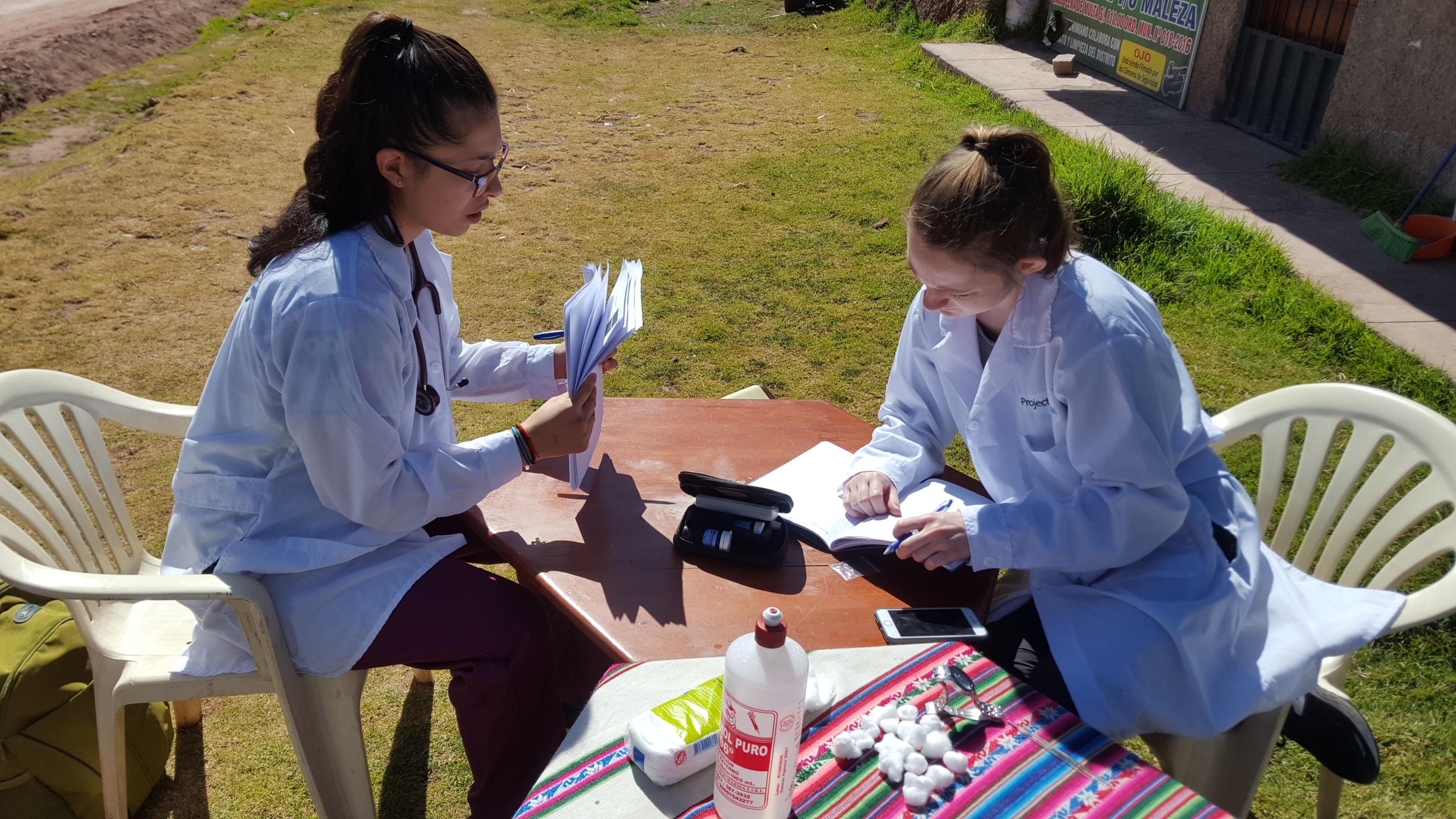 Dos pasantes de enfermería revisando información de pacientes en Perú. Par de estudiantes en una pasantía de nutrición revisando información de pacientes durante una brigada en Perú.